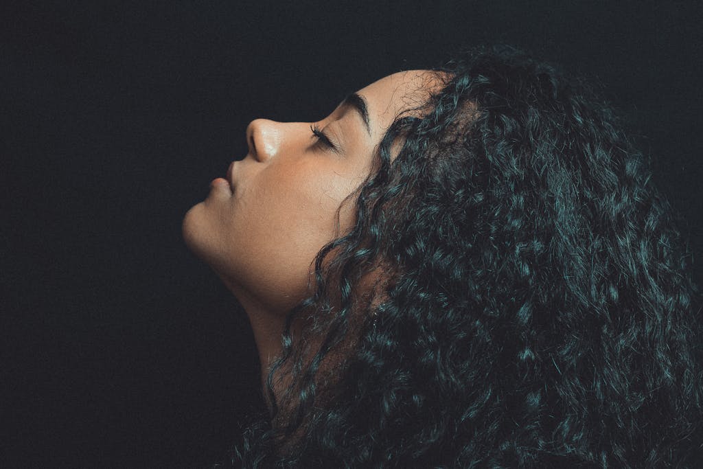 Artistic side profile portrait of a woman with curly hair in dramatic lighting.