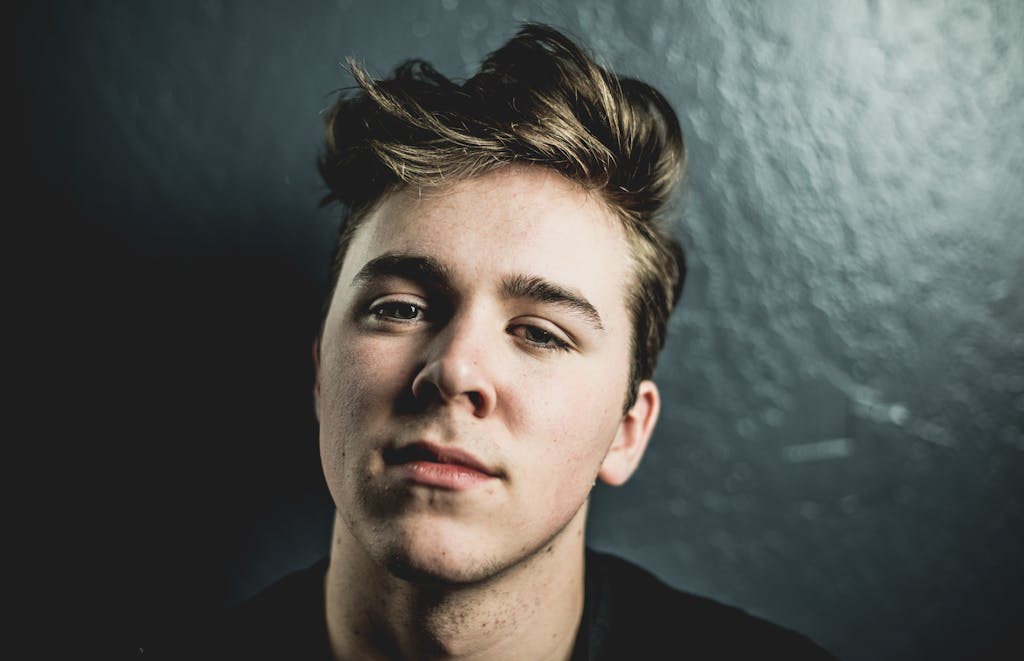 Close-up portrait of a young man with a serious expression against a textured dark background.